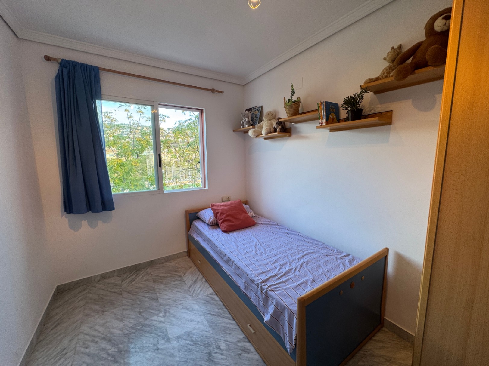 Eenpersoonskamer met marmeren vloer, houten wandplanken en een schuifraam met uitzicht op groen. Het bed is voorzien van geïntegreerde opbergladen.