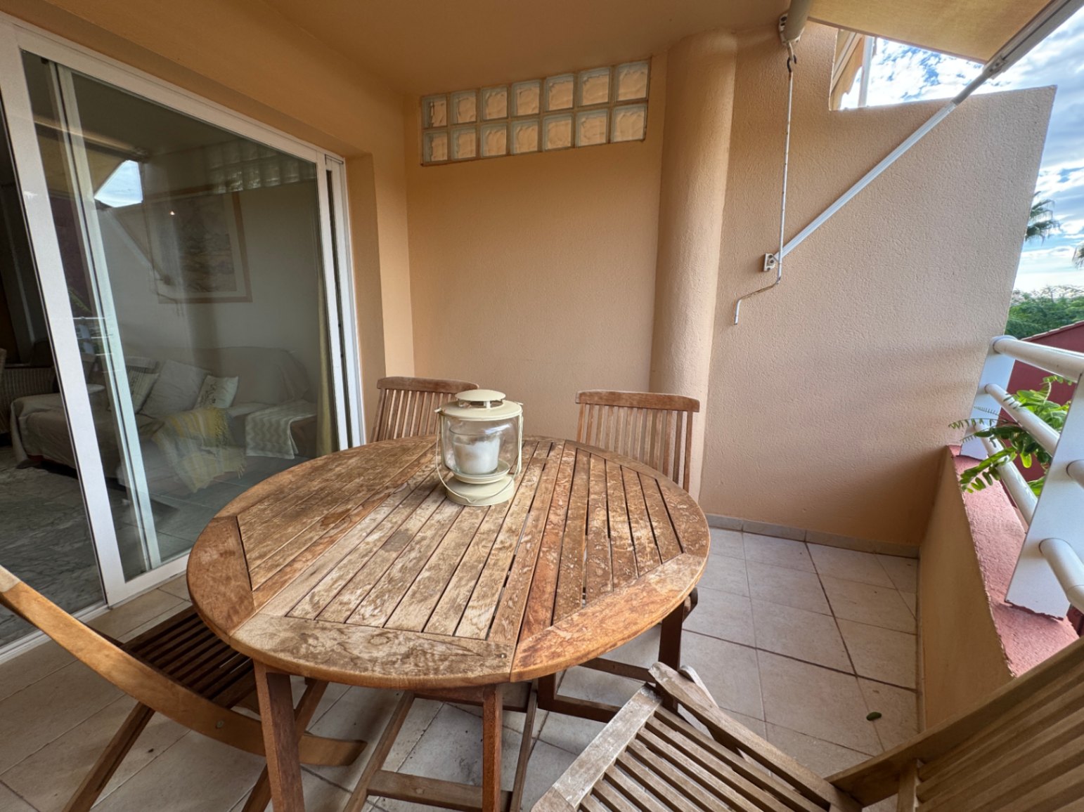 Overdekt terras met een ronde houten eethoek en tegelvloer, bereikbaar via grote glazen schuifdeuren vanuit de woonkamer.