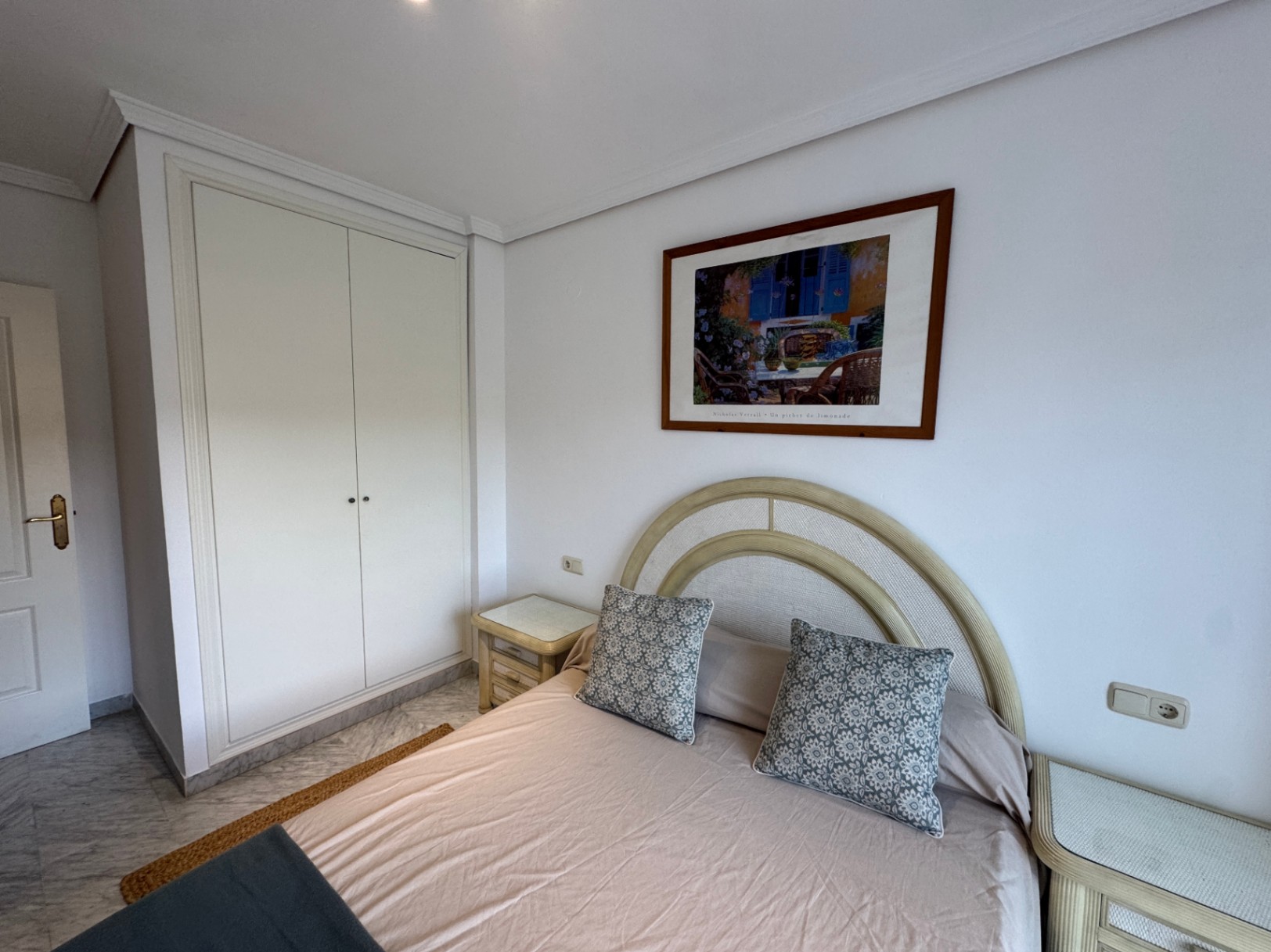 Slaapkamer met witte inbouwkast, marmeren vloer en een bed met een gebogen hoofdbord geflankeerd door bijpassende nachtkastjes.