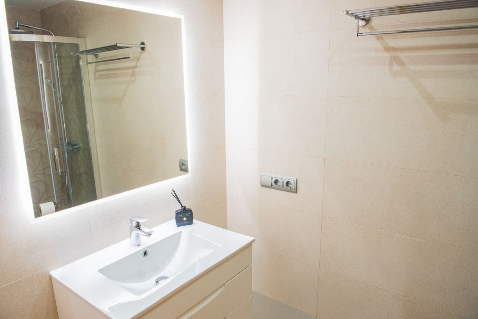 Moderne badkamer met wit wastafelmeubel, spiegel met geïntegreerde ledverlichting en wanden met beige keramische tegels.