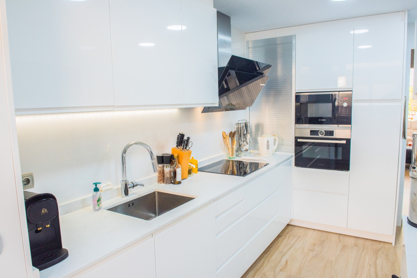 Moderne keuken met witte hoogglans kasten, geïntegreerde Bosch-apparatuur en een wit kwarts werkblad met inductiekookplaat en schuine afzuigkap.