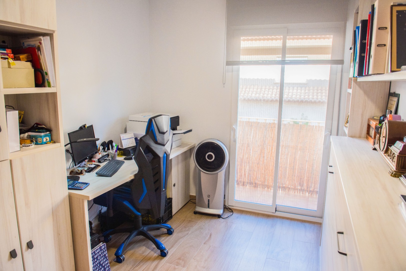 Werkkamer met lichthouten bureau, ergonomische stoel en ingebouwde kasten. Een glazen schuifdeur zorgt voor natuurlijk licht en biedt toegang tot een balkon.