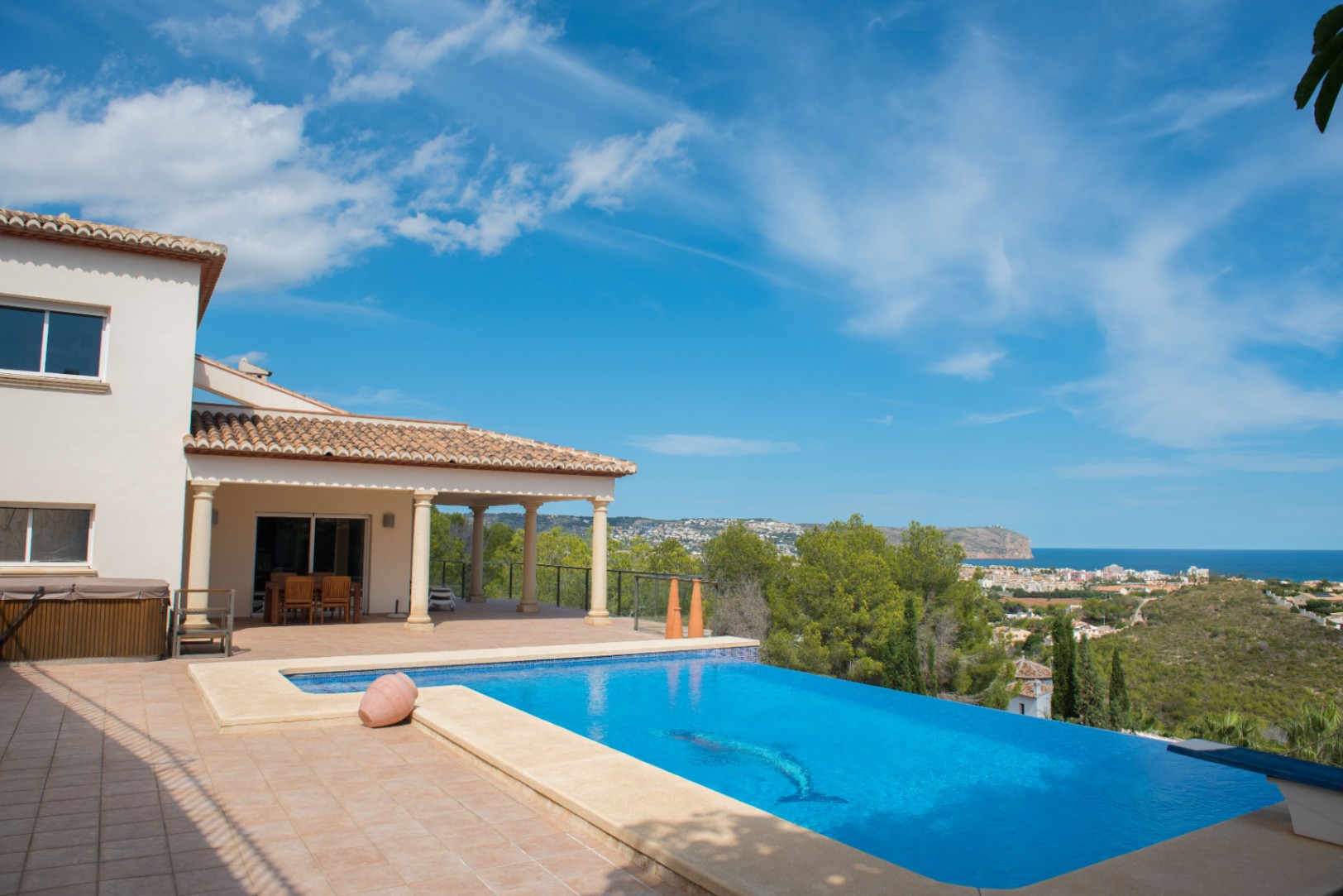 Infinity-zwembad met dolfijnmozaïek en panoramisch uitzicht op zee. De villa heeft een overdekt terras met stenen zuilen en een dak van terracotta pannen.