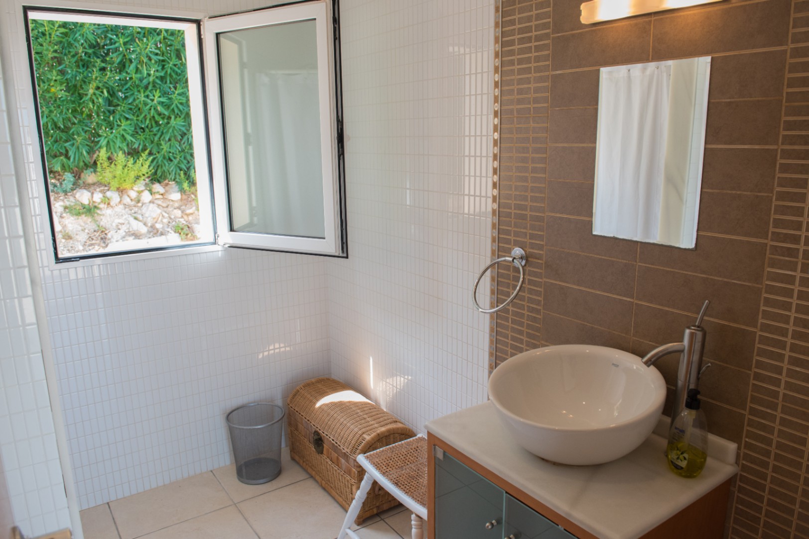 Moderne badkamer met een opzetwastafel, bruine accentmuur en een open raam met uitzicht op de omliggende tuin en natuurlijke lichtinval.