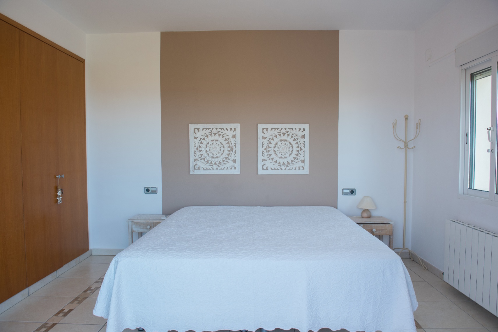 Slaapkamer met taupe accentmuur, wit houtgesneden wandpanelen, houten inbouwkast en tegelvloer met decoratieve rand.