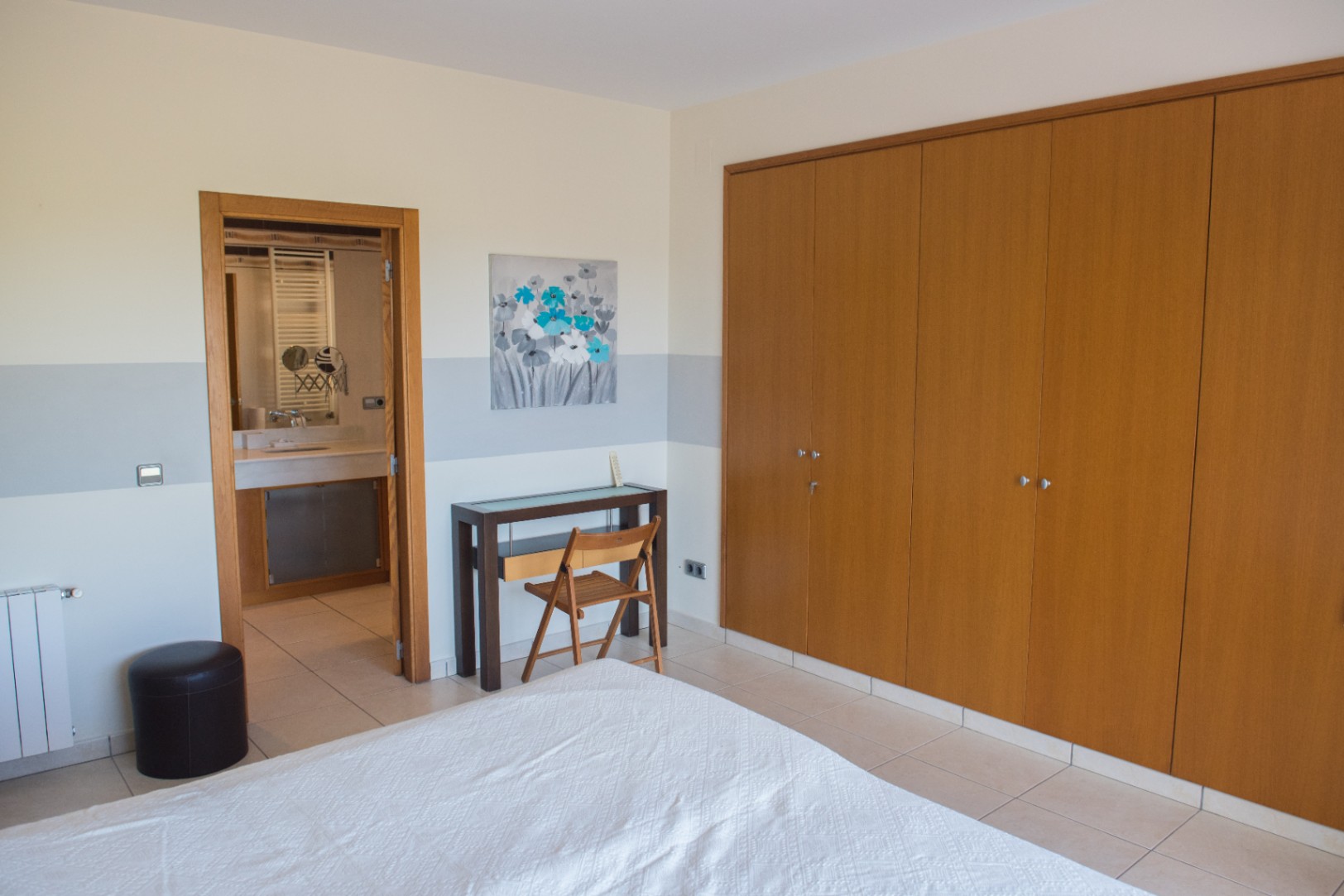Slaapkamer voorzien van een grote houten inbouwkast, een compacte werkplek en toegang tot een aangrenzende badkamer.