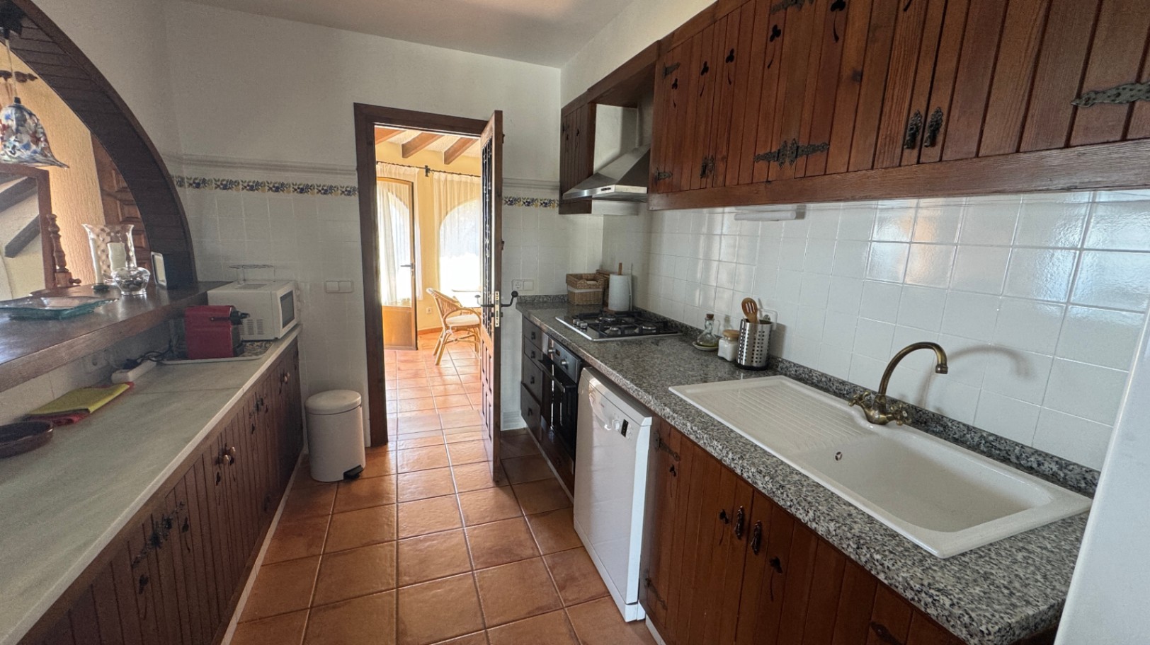 Rustieke keuken met donkerhouten kasten, granieten werkbladen en terracotta vloertegels. Voorzien van een gaskookplaat en een ronde doorgeefopening.