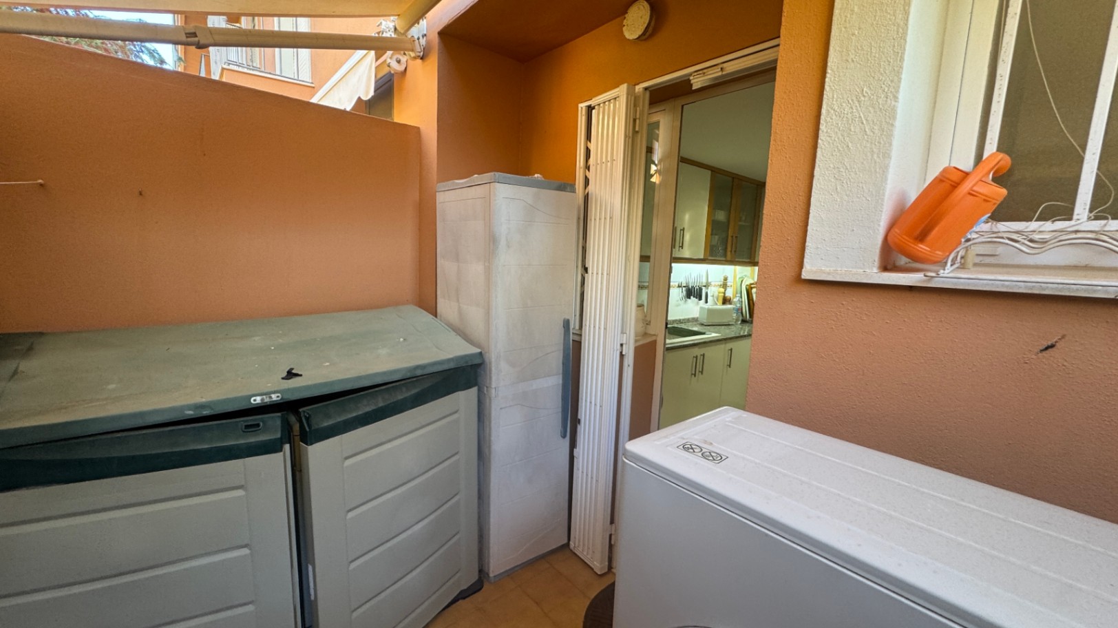 Bijkeuken-terras met terracotta muren, opbergkasten voor buiten en directe toegang tot de keuken via een vouwdeur.