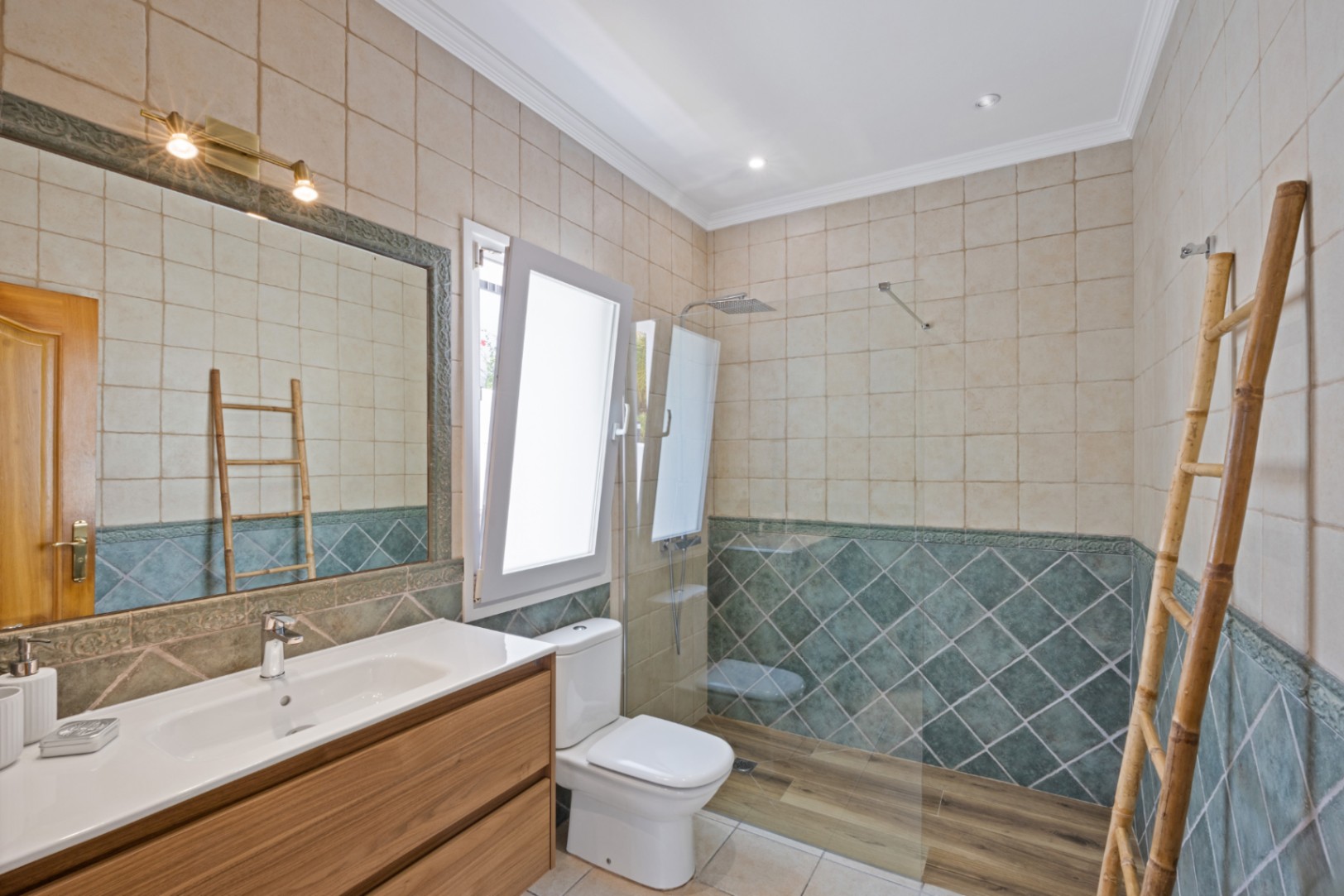 Badkamer met inloopdouche voorzien van houtlook vloer, groene ruitvormige wandtegels, houten wastafelmeubel en een decoratieve bamboe ladder.