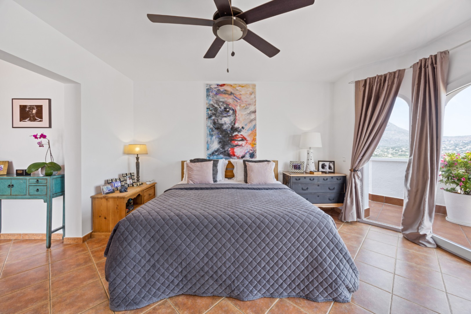 Lichte slaapkamer met terracotta tegelvloer, plafondventilator en glazen schuifdeuren naar een privébalkon met panoramisch uitzicht op de bergen.
