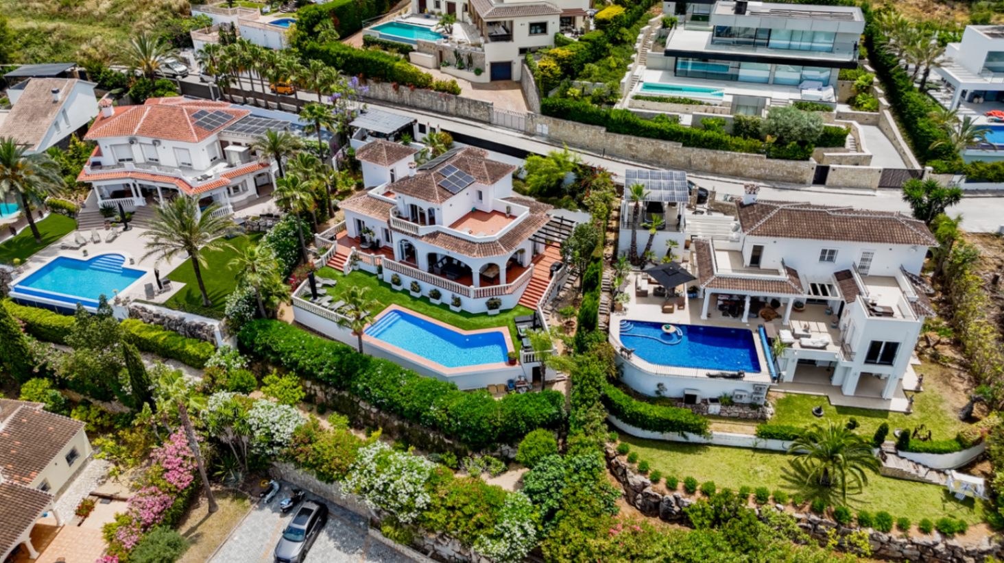 Luchtfoto van luxe mediterrane villa's met privézwembaden, terracotta daken, zonnepanelen en verzorgde tuinen op een heuvelachtige locatie.