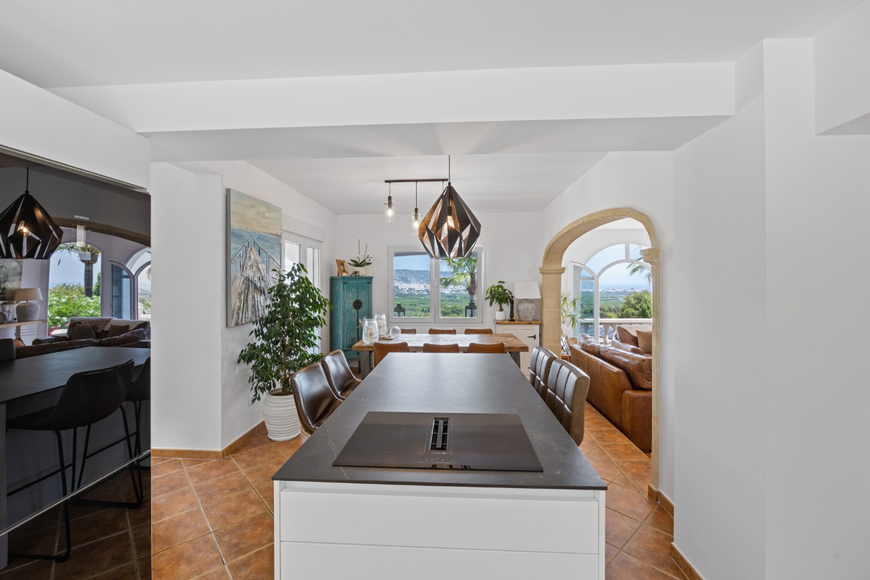 Modern kookeiland met inductiekookplaat en afzuigsysteem, terracotta vloer en een stenen boog die leidt naar de woonkamer met panoramisch uitzicht op de vallei.