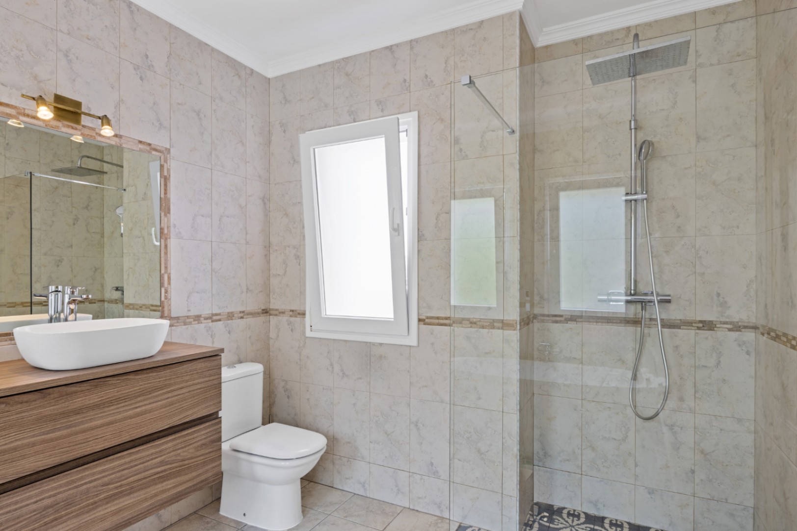Moderne badkamer met inloopdouche, glazen wand, zwevend houten wastafelmeubel met opzetkom en beige tegels met marmerlook en natuurlijk licht.