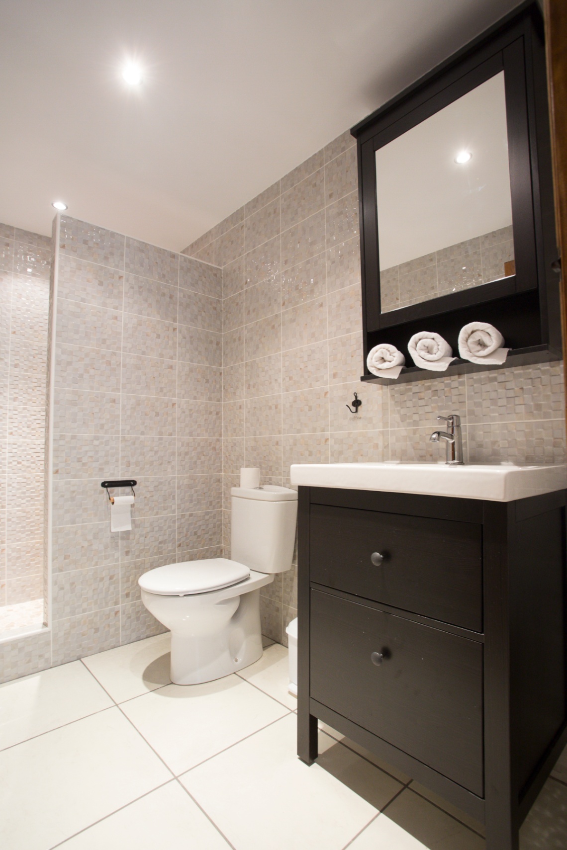 Moderne badkamer met beige mozaïektegels, een donkerhouten wastafelmeubel en een bijpassende spiegelkast voorzien van handdoekopslag.