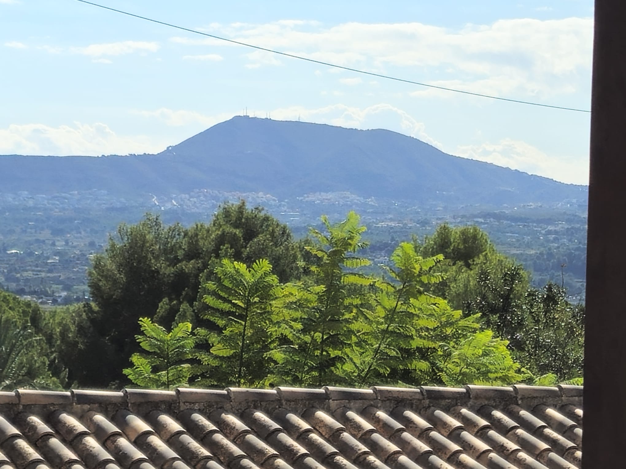 Panoramisch uitzicht vanaf het dak met traditionele dakpannen, weelderig groen en een prominente berg aan de horizon onder een heldere hemel.