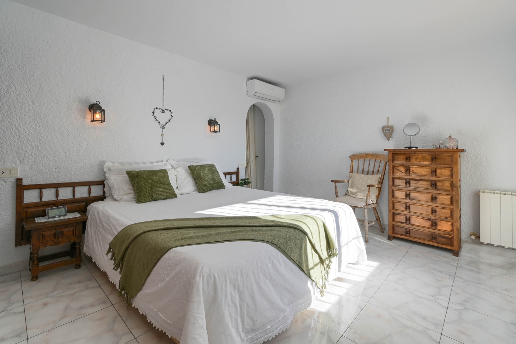 Slaapkamer met witte structuurwanden, marmeren vloer en rustieke houten meubels. Voorzien van wandlantaarns en textiel met groene accenten.