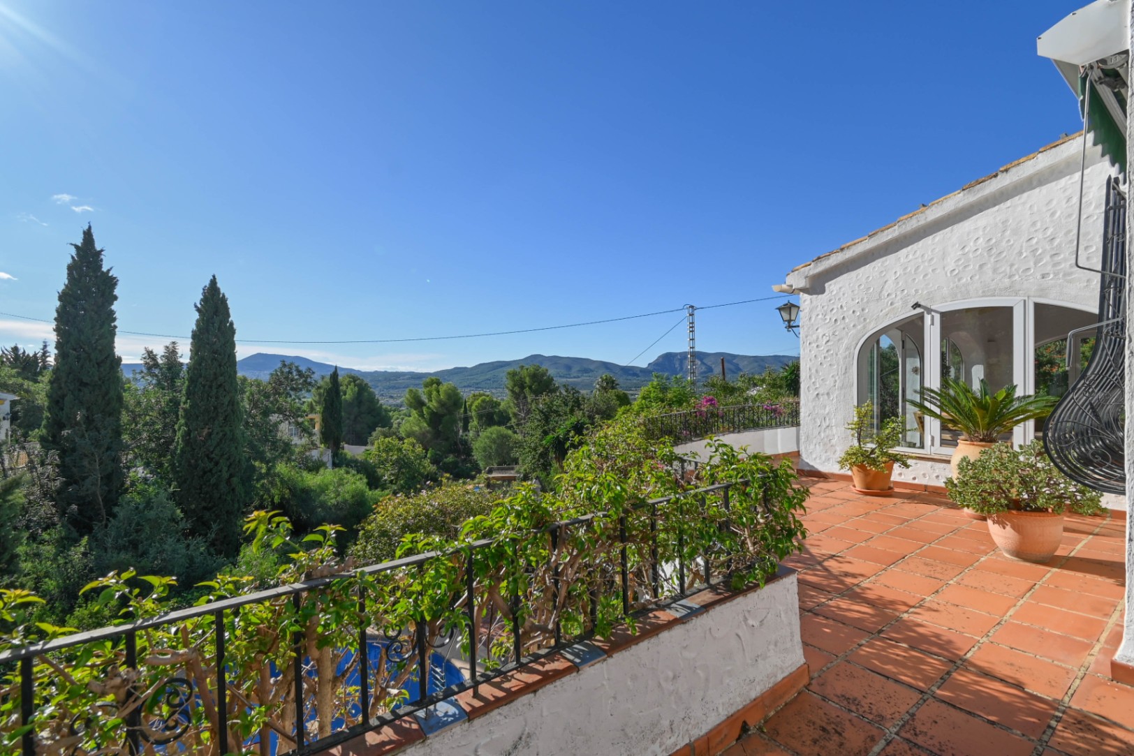 Verhoogd terras met terracotta tegels en smeedijzeren balustrade, met panoramisch uitzicht over de omliggende bergen en de groene vallei.