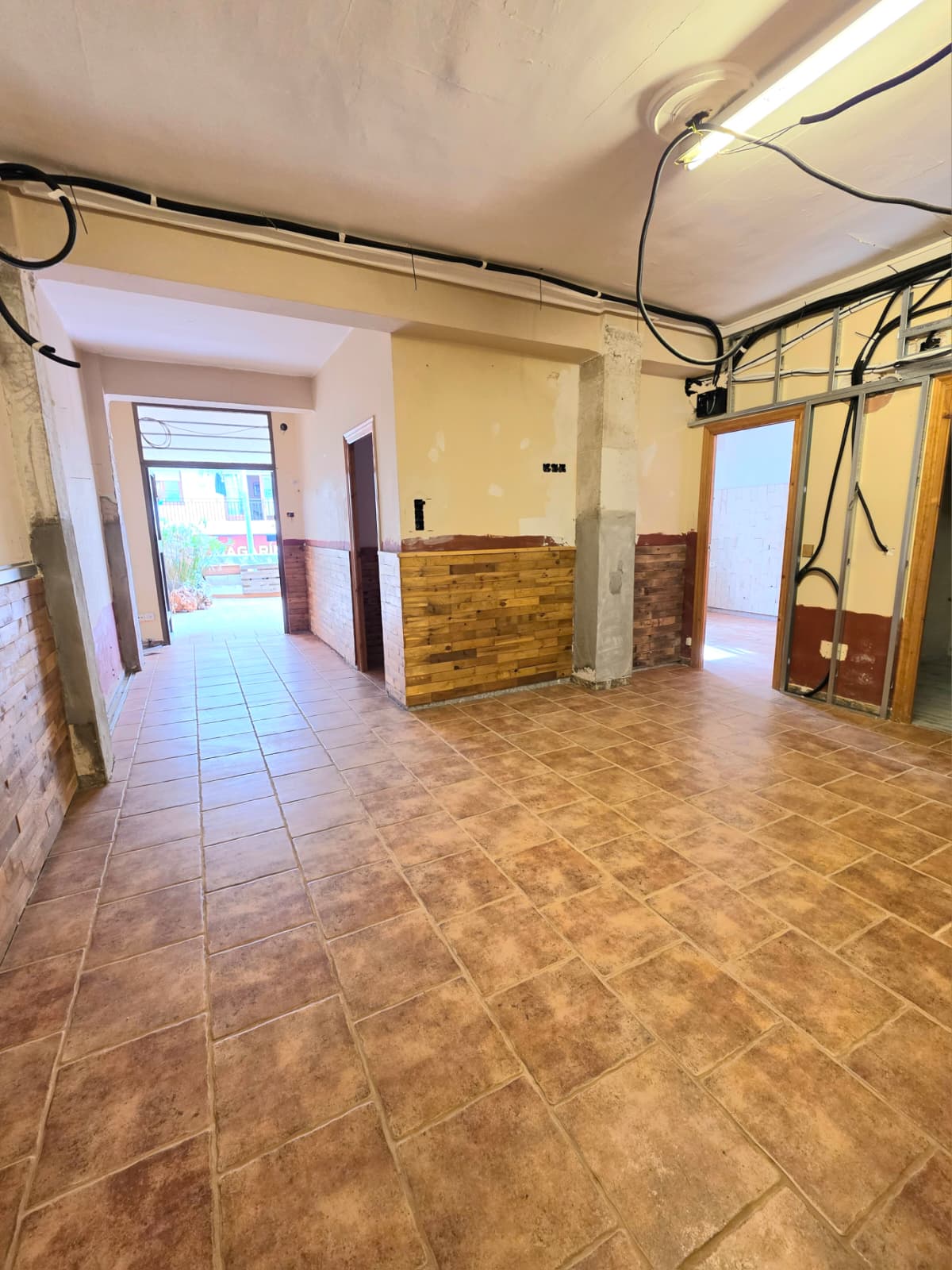 Binnenruimte in renovatie met terracotta vloertegels, houten wandbekleding en zichtbare elektrische bedrading en metalen profielen.