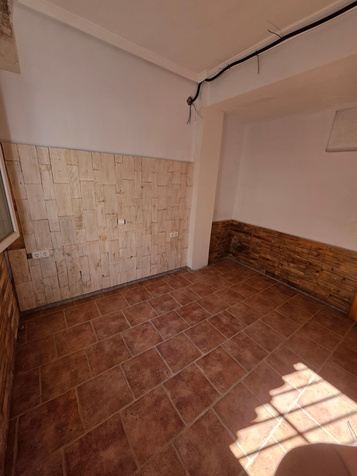 Binnenruimte met terracotta tegelvloer en een decoratieve wand van lichtgekleurde houten planken. Voorzien van zichtbare bedrading en stopcontacten.