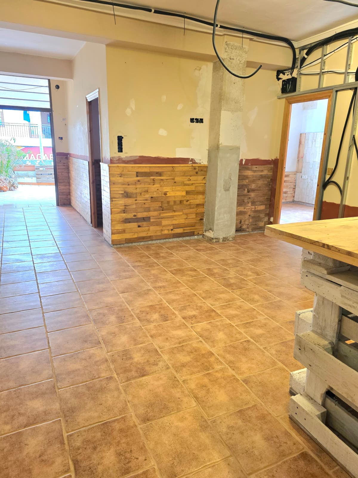 Binnenruimte met terracotta vloertegels, rustieke houten lambrisering en zichtbare plafondbedrading, klaar voor verdere afwerking of renovatie.