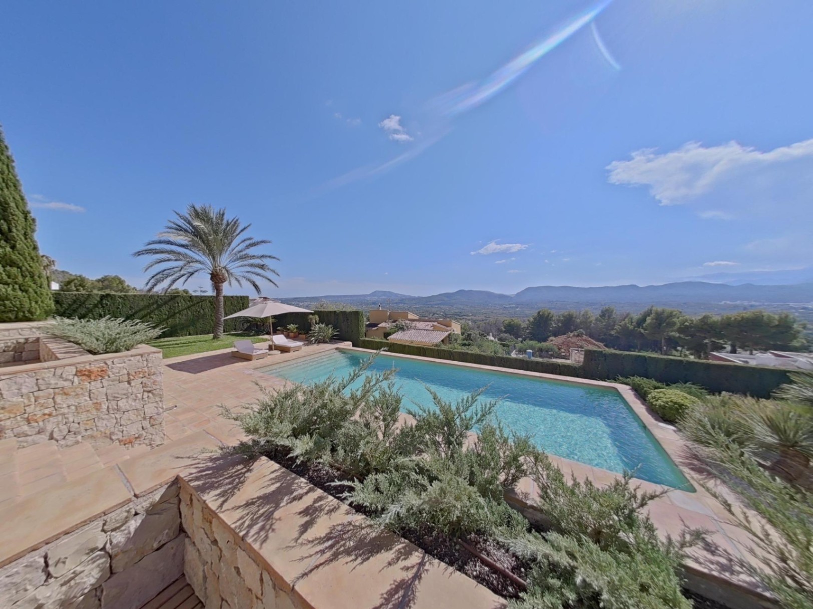 Buitenzwembad met stenen terras en panoramisch uitzicht over de vallei. Voorzien van ligbedden, een palmboom en mediterrane beplanting.