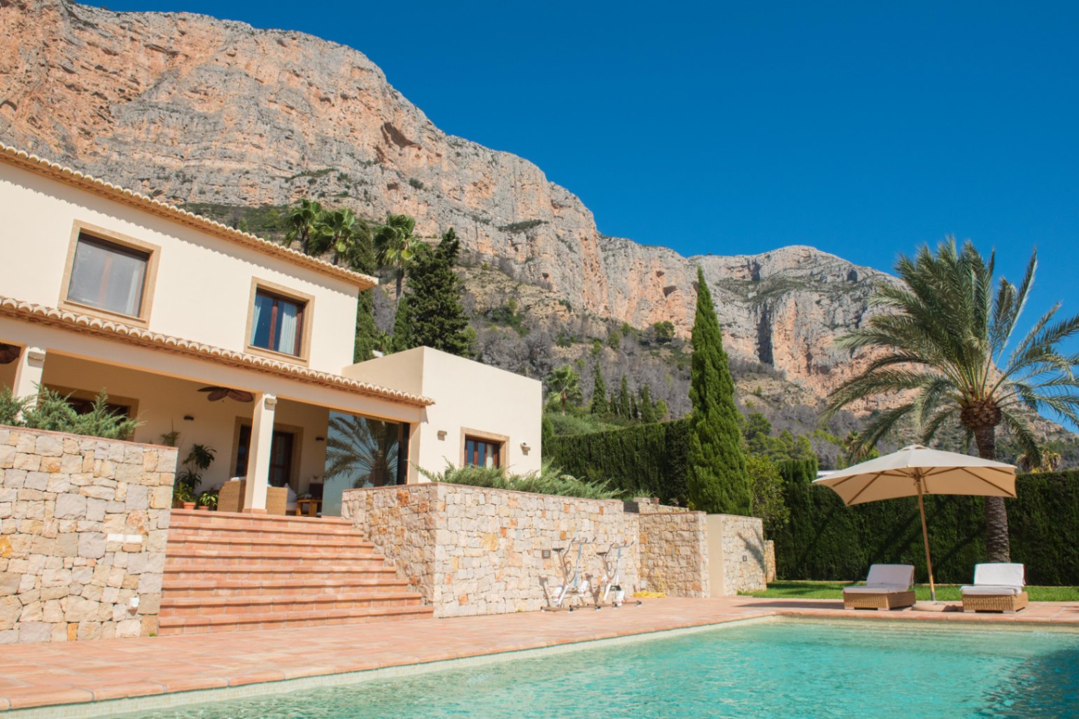 Exterieur met turquoise zwembad, terracotta terras en natuurstenen muren tegen een indrukwekkend berglandschap met mediterrane beplanting.