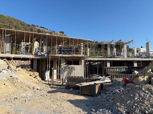 Ruwbouw van een moderne villa met kolommen van gewapend beton, metalen stempels en houten bekisting op een bergachtige locatie.