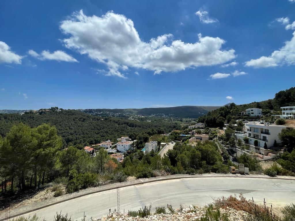 Verhoogd panoramisch uitzicht op een mediterrane vallei met witte villa's tussen dennenheuvels onder een helderblauwe lucht met witte wolken.