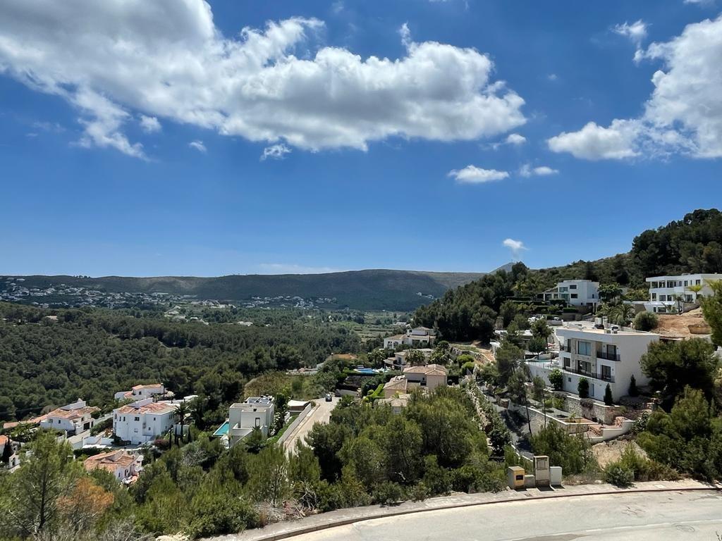 Verhoogd uitzicht over een mediterrane vallei met witte villa's te midden van dichte dennenbossen onder een blauwe lucht.