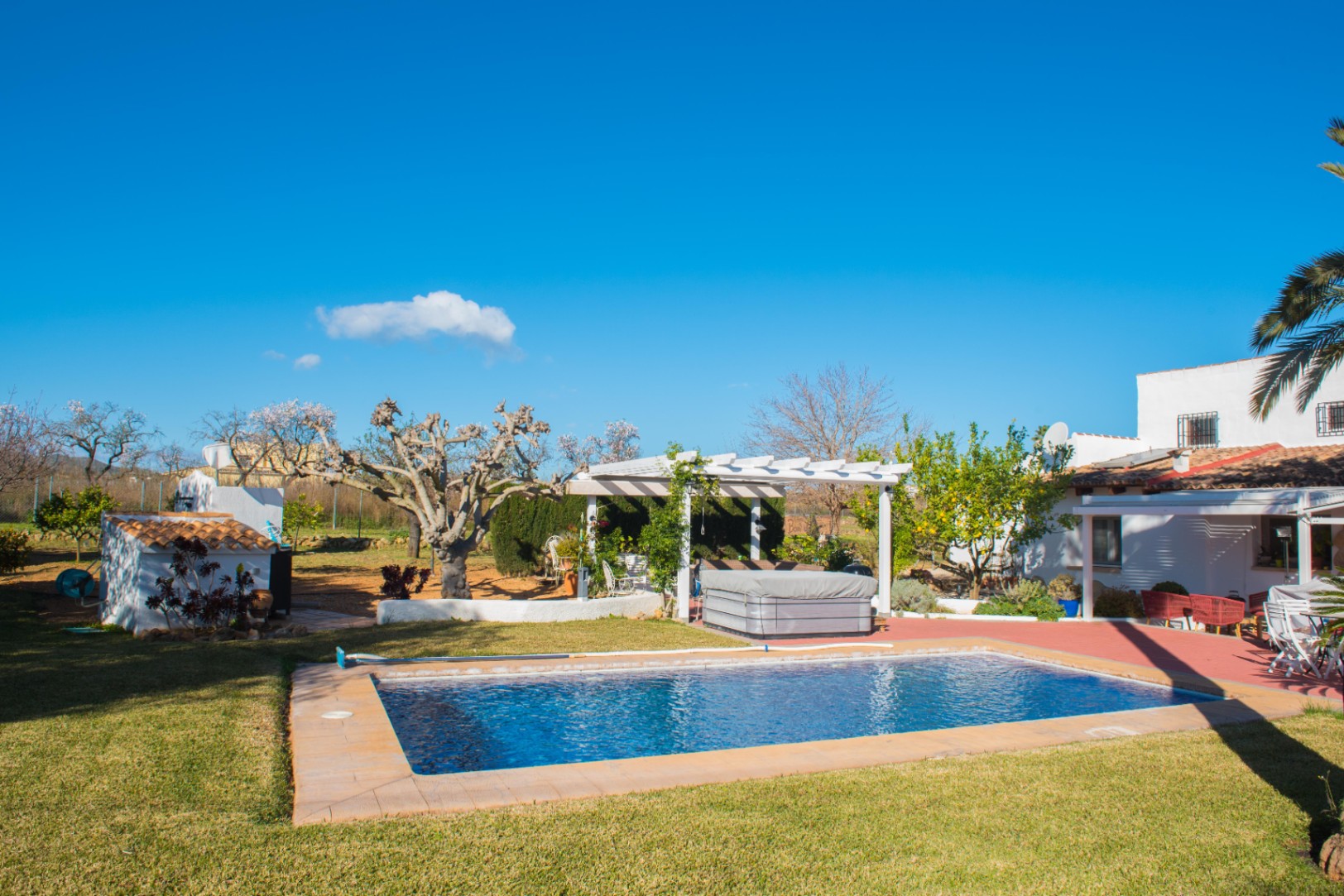 Buitenruimte met een rechthoekig zwembad, een verzorgd gazon en een witte pergola met een hottub, grenzend aan een mediterrane villa.