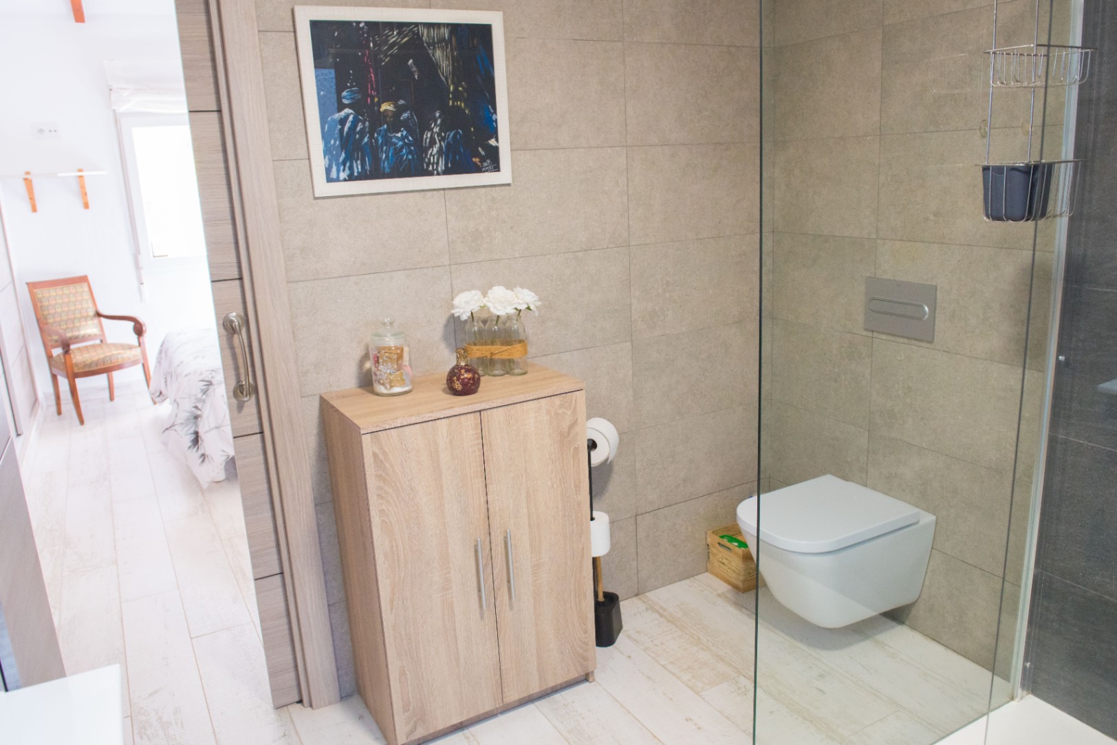 Moderne badkamer met hangend toilet, glazen douchewand en een licht houten opbergkast tegen neutrale wandtegels met steeneffect.