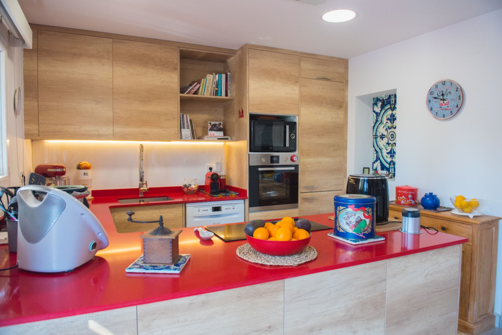 Moderne keuken met een opvallend rood werkblad, lichte houten kasten en inbouwapparatuur waaronder een oven en inductiekookplaat.