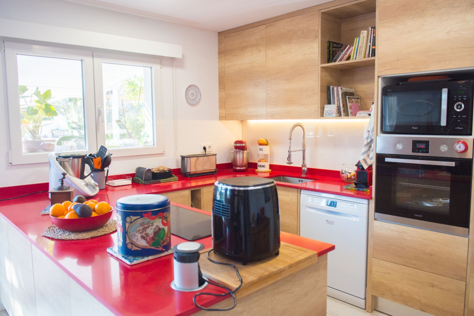 Moderne keuken met een opvallend rood werkblad, lichte houten kasten en inbouwapparatuur waaronder een oven, magnetron en vaatwasser.