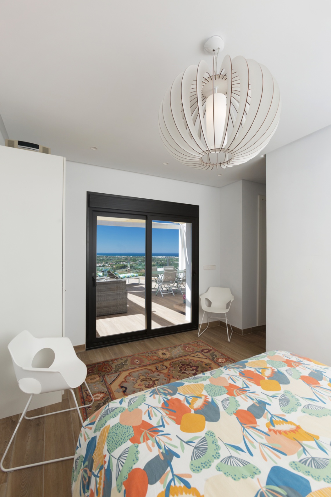 Lichte slaapkamer met directe toegang tot het terras via zwarte schuifdeuren, voorzien van een design hanglamp en panoramisch uitzicht op zee.