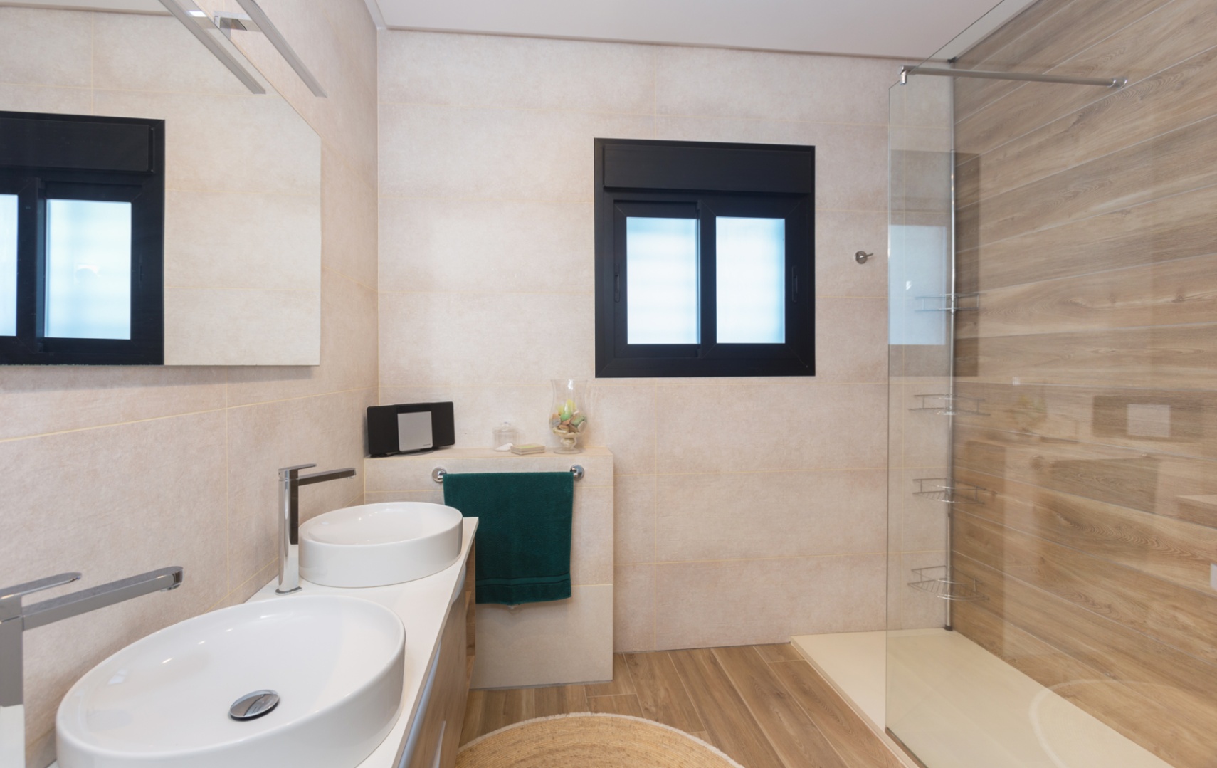 Moderne badkamer met dubbele opzetwastafel, houtlook tegels op de vloer en in de douche, en een glazen wand naast een raam met zwart kozijn.