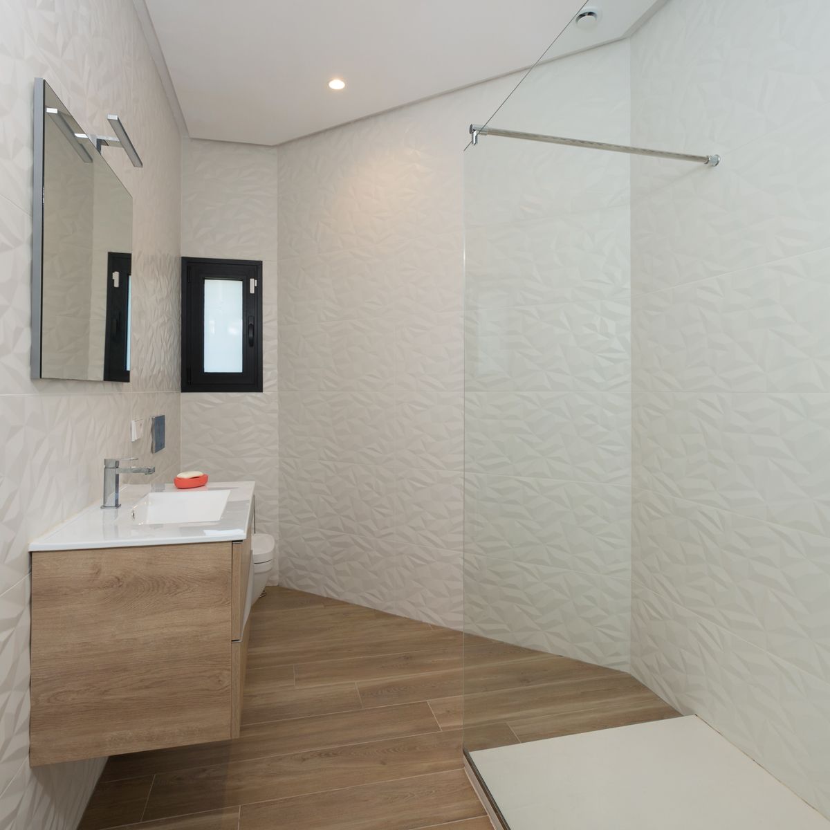 Moderne badkamer met geometrische reliëftegels, een zwevend houten wastafelmeubel en een inloopdouche met een glazen wandpaneel.