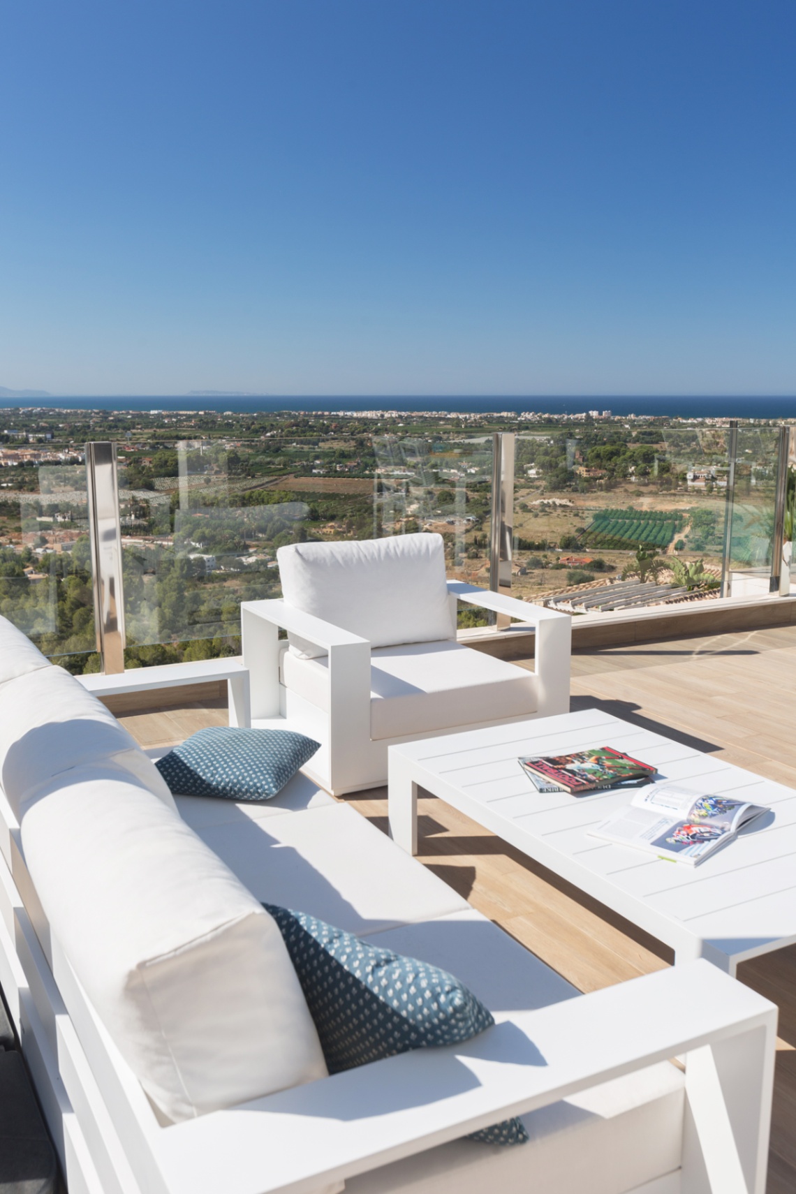 Terras met modern wit loungemeubilair en glazen balustrades, met panoramisch uitzicht over het kustlandschap en de Middellandse Zee.