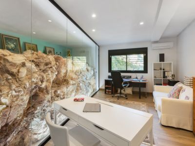 Kantoor met een natuurlijke rotswand achter een glazen scheidingswand, wat een unieke werkruimte creëert. Voorzien van twee bureaus en een bank.