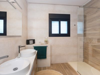 Moderne badkamer met dubbele ovale wastafel, chromen kranen en verlichte spiegel. De inloopdouche heeft een glazen wand, hout-effect tegels en een bijpassende tegelvloer.
