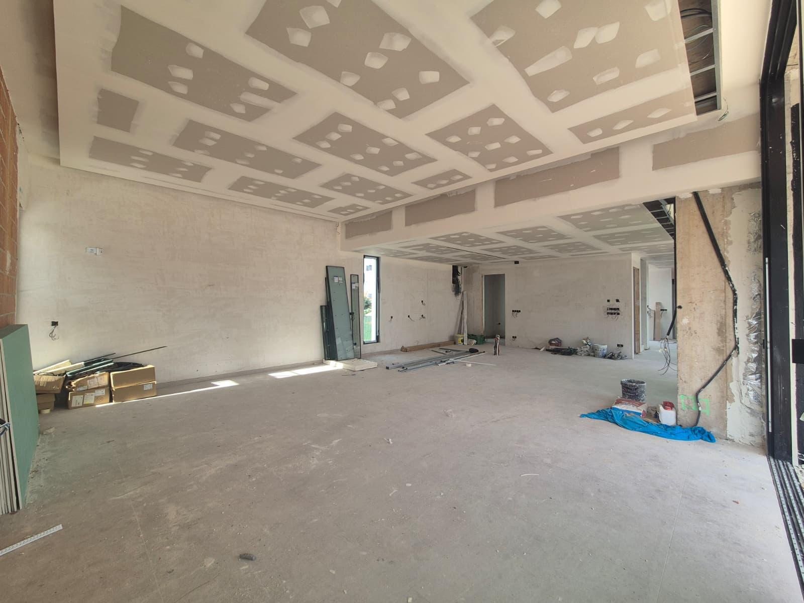 Ruim interieur in aanbouw met verlaagde gipsplaten plafonds voor indirecte verlichting en grote openingen voor kamerhoge ramen.