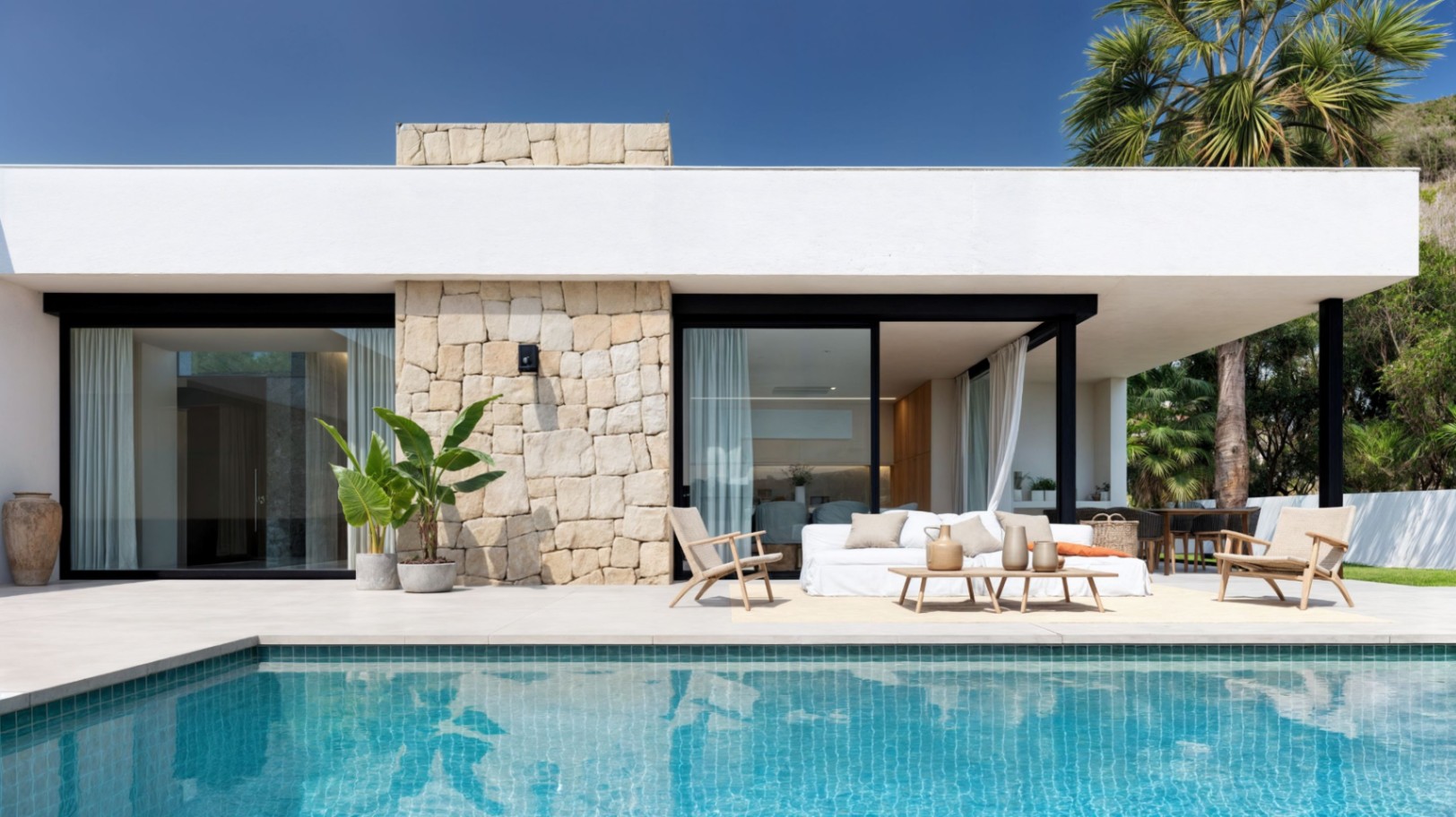 Modern exterieur met een turquoise zwembad, natuurstenen wanden en een loungegedeelte op een ruim terras met grote keramische tegels.