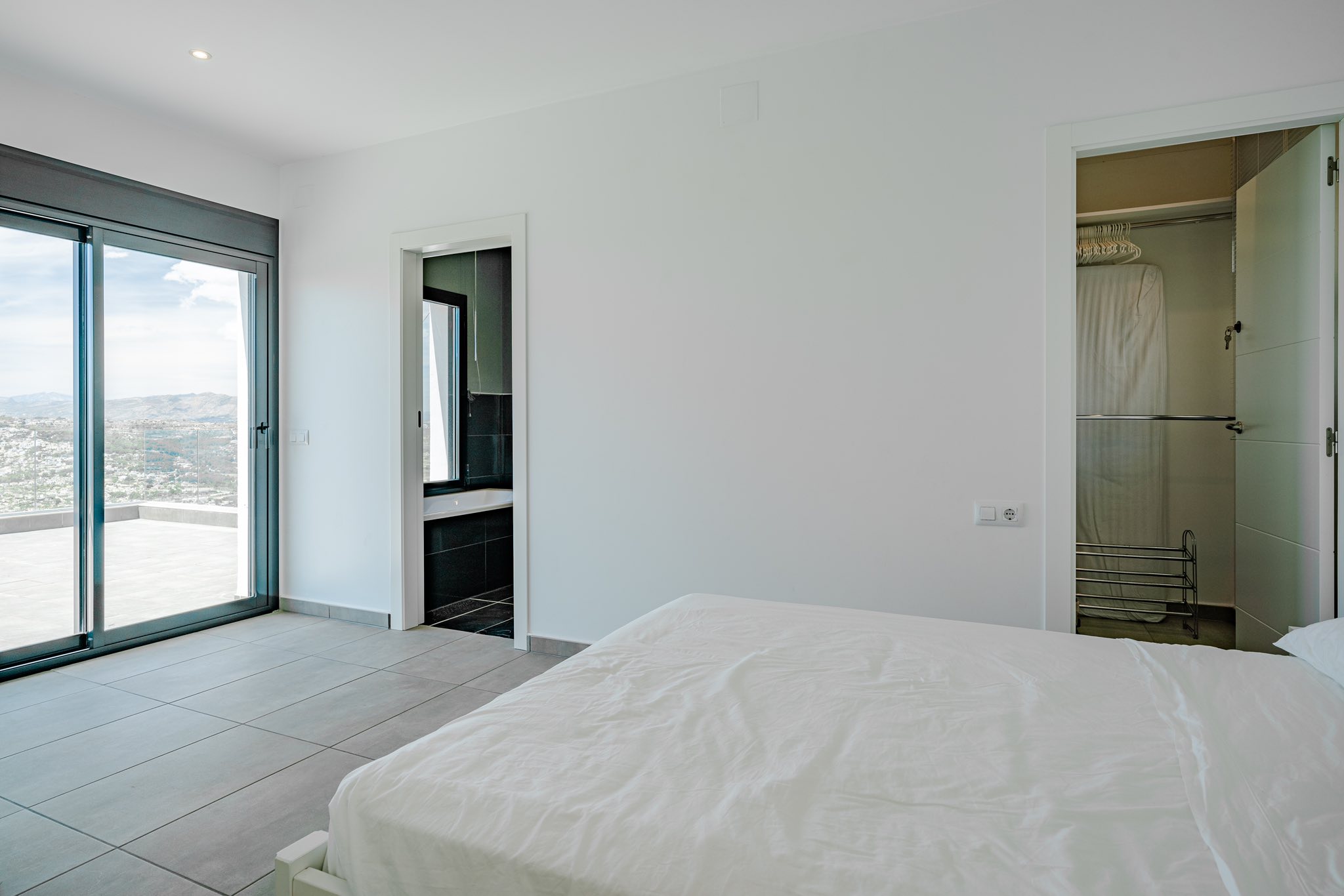 Moderne slaapkamer met schuifpui naar het terras, en-suite badkamer met donkere tegels en een praktische, aangrenzende inloopkast.