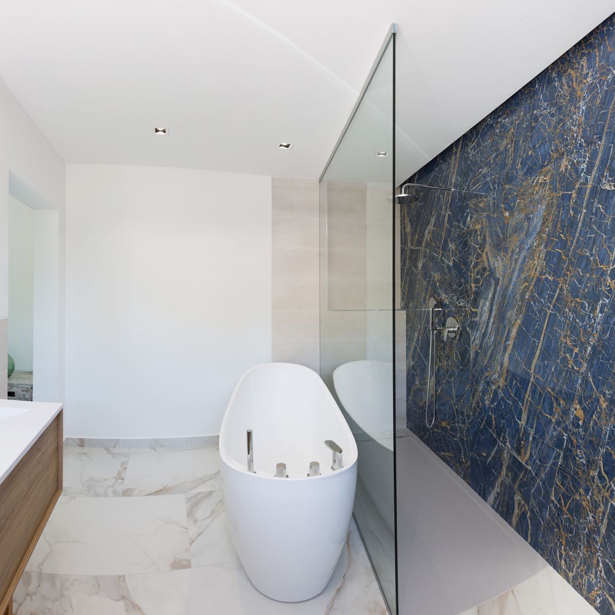 Moderne badkamer met vrijstaand ovaal bad, inloopdouche met blauwe marmeren wand en witte marmeren vloer met gouden aders.