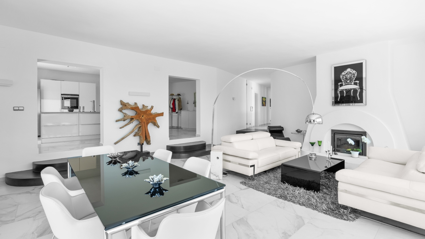 Open woon- en eetkamer met marmeren vloer, witte lederen banken, een moderne haard en glazen eettafel met doorkijk naar de strakke witte keuken.