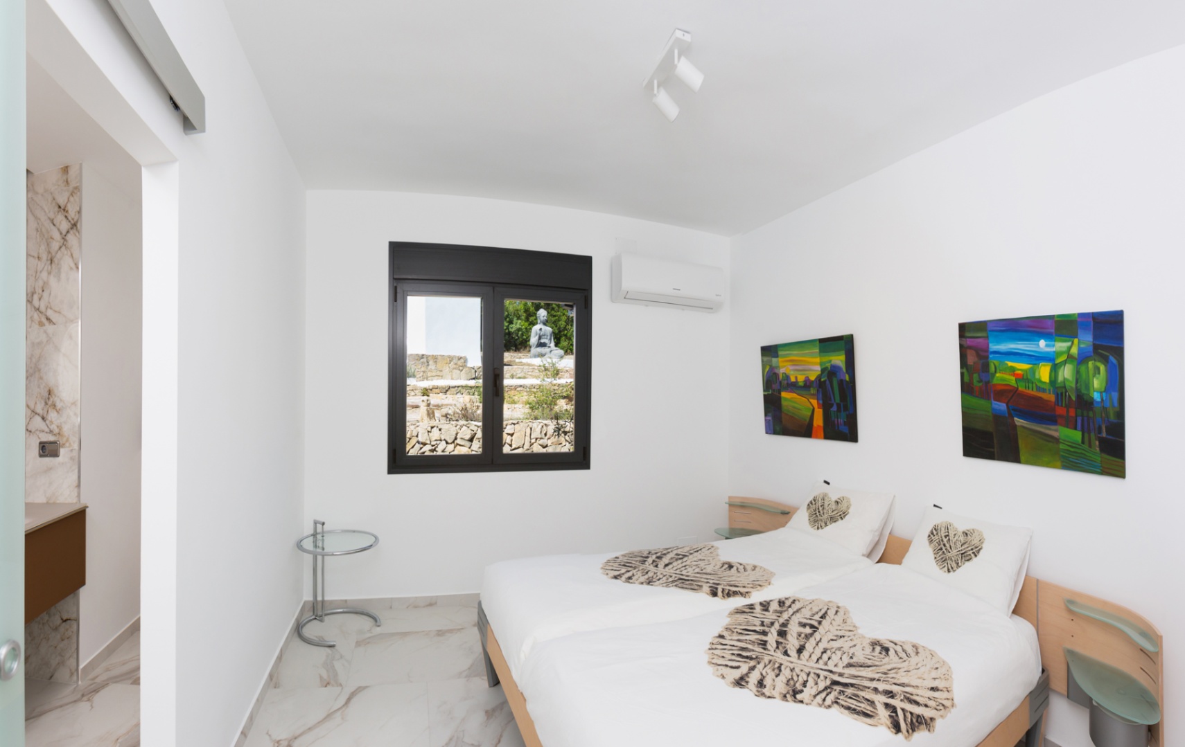 Slaapkamer met twee eenpersoonsbedden, marmerlook vloertegels en raam met uitzicht op een rotstuin. Voorzien van airconditioning en toegang tot een ensuite badkamer.