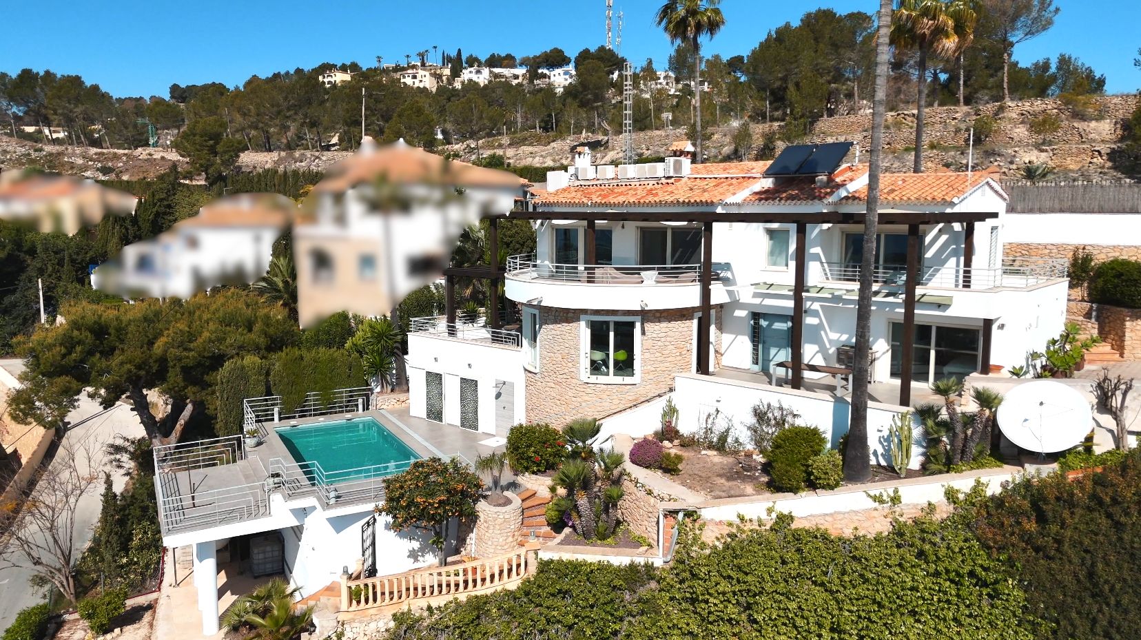 Mediterrane villa met meerdere niveaus, witte gevel, stenen accenten, zonnepanelen en een privézwembad te midden van een tuin met palmbomen.