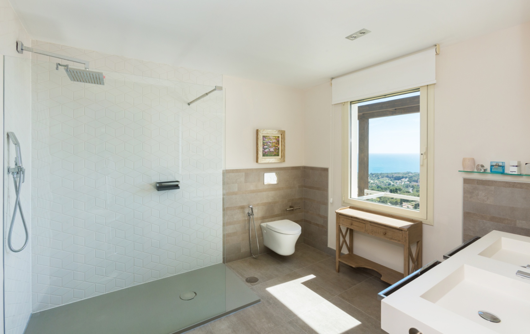 Moderne badkamer met inloopdouche voorzien van zeshoekige tegels, dubbele wastafel en een groot raam met panoramisch uitzicht op zee.