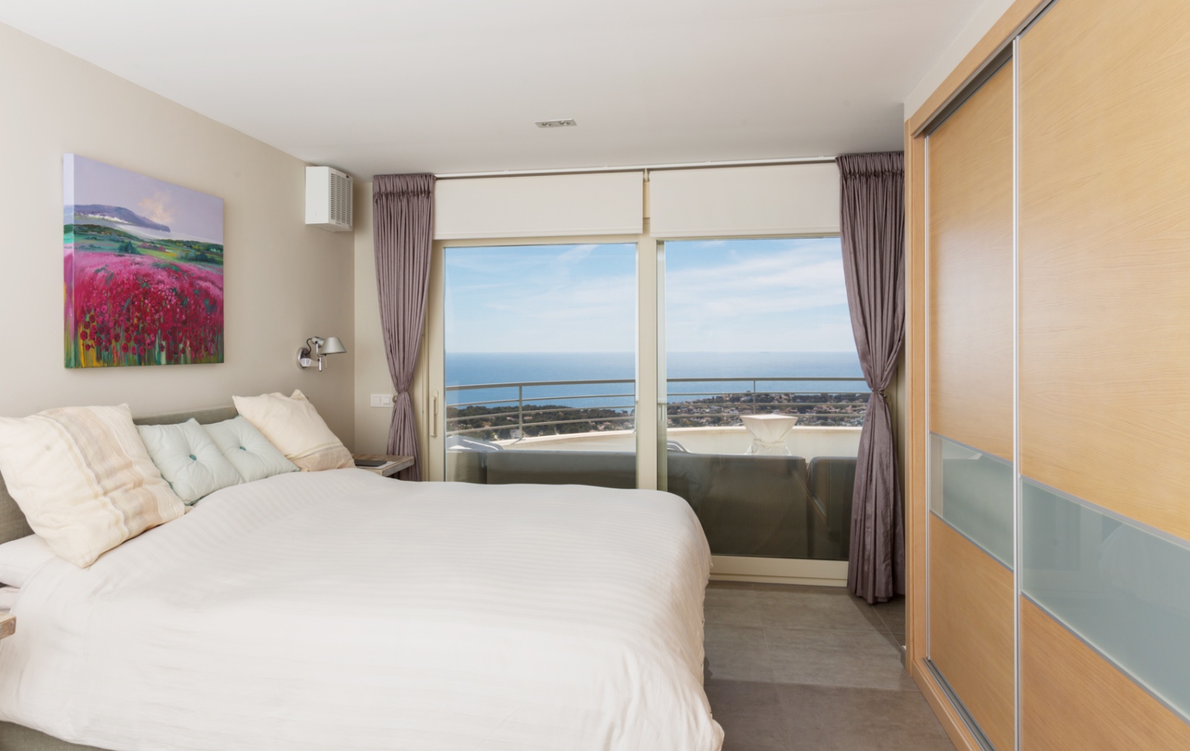 Moderne slaapkamer met houten inbouwkast en kamerhoge glazen deuren die toegang bieden tot een terras met weids uitzicht op zee.