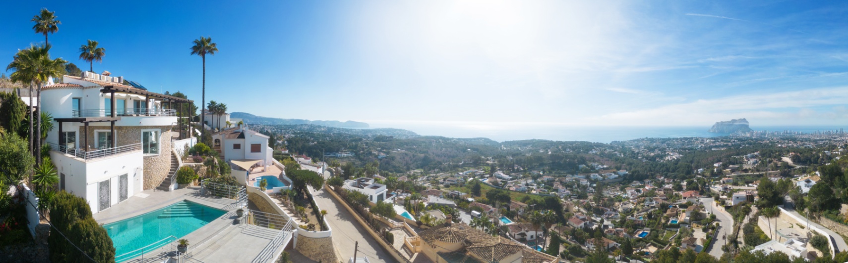 Panoramisch uitzicht op een mediterrane villa met privézwembad, natuurstenen gevels en ruime terrassen met uitzicht op de kustlijn en de Peñón de Ifach.