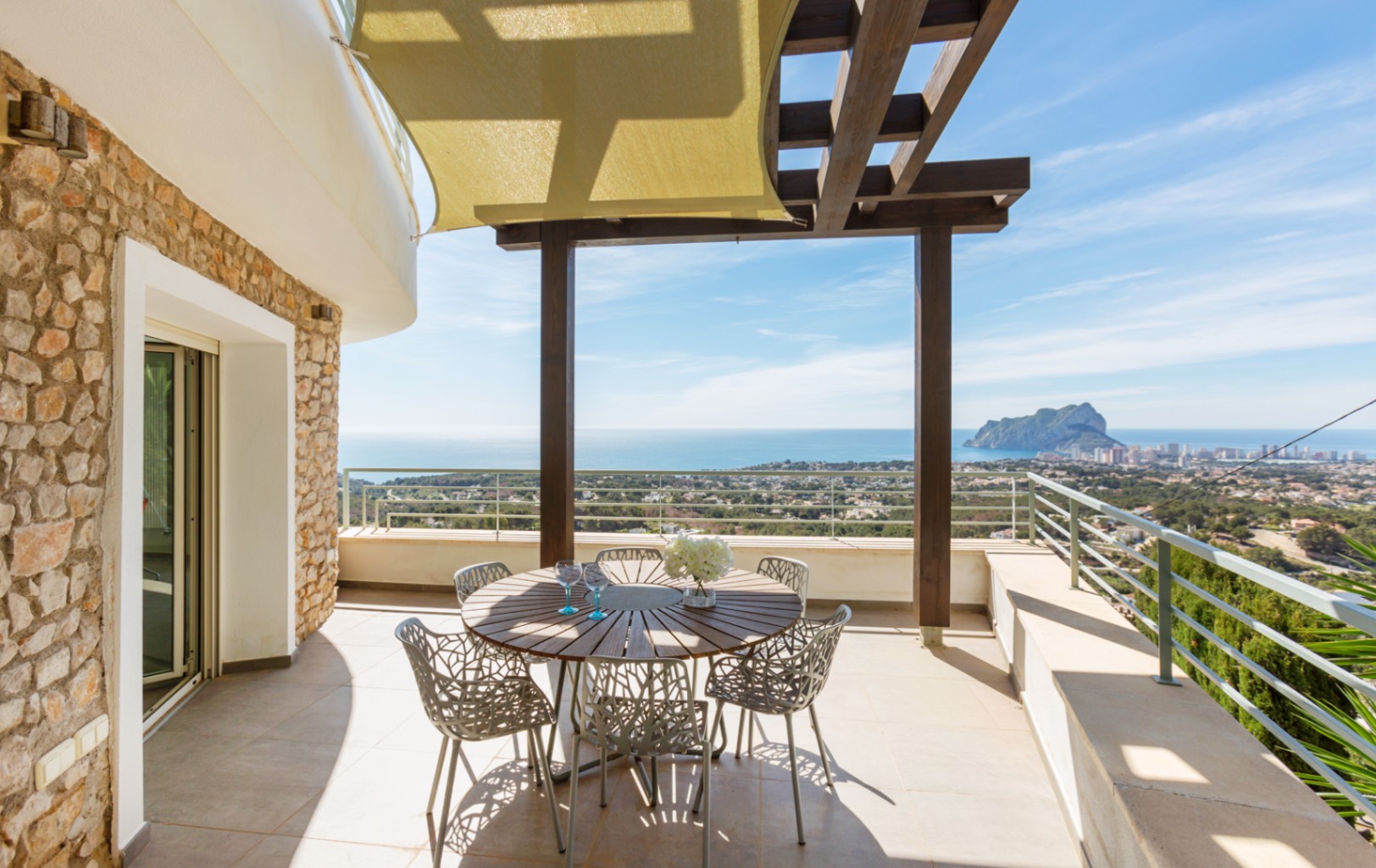 Terras met natuurstenen muren, een houten pergola en schaduwdoek. Buiten eethoek met panoramisch uitzicht op de Middellandse Zee en de Peñón de Ifach.